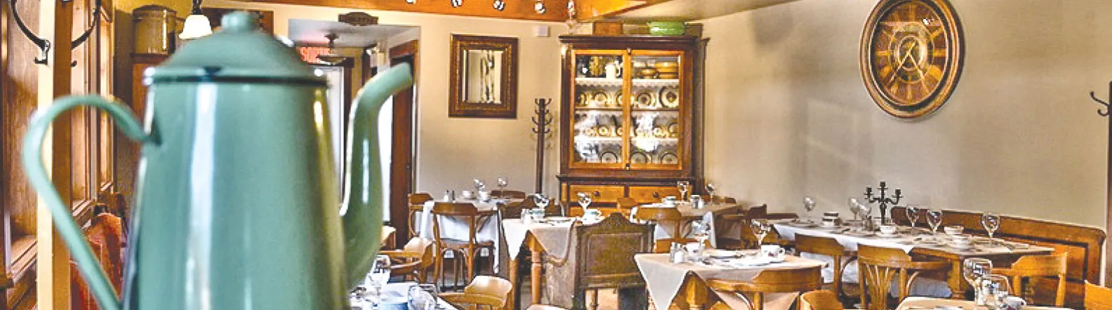 Salle à manger du Citron Vert : tables nappées, chaises de bois, vaisselier ancien et cafetière émaillée au premier plan